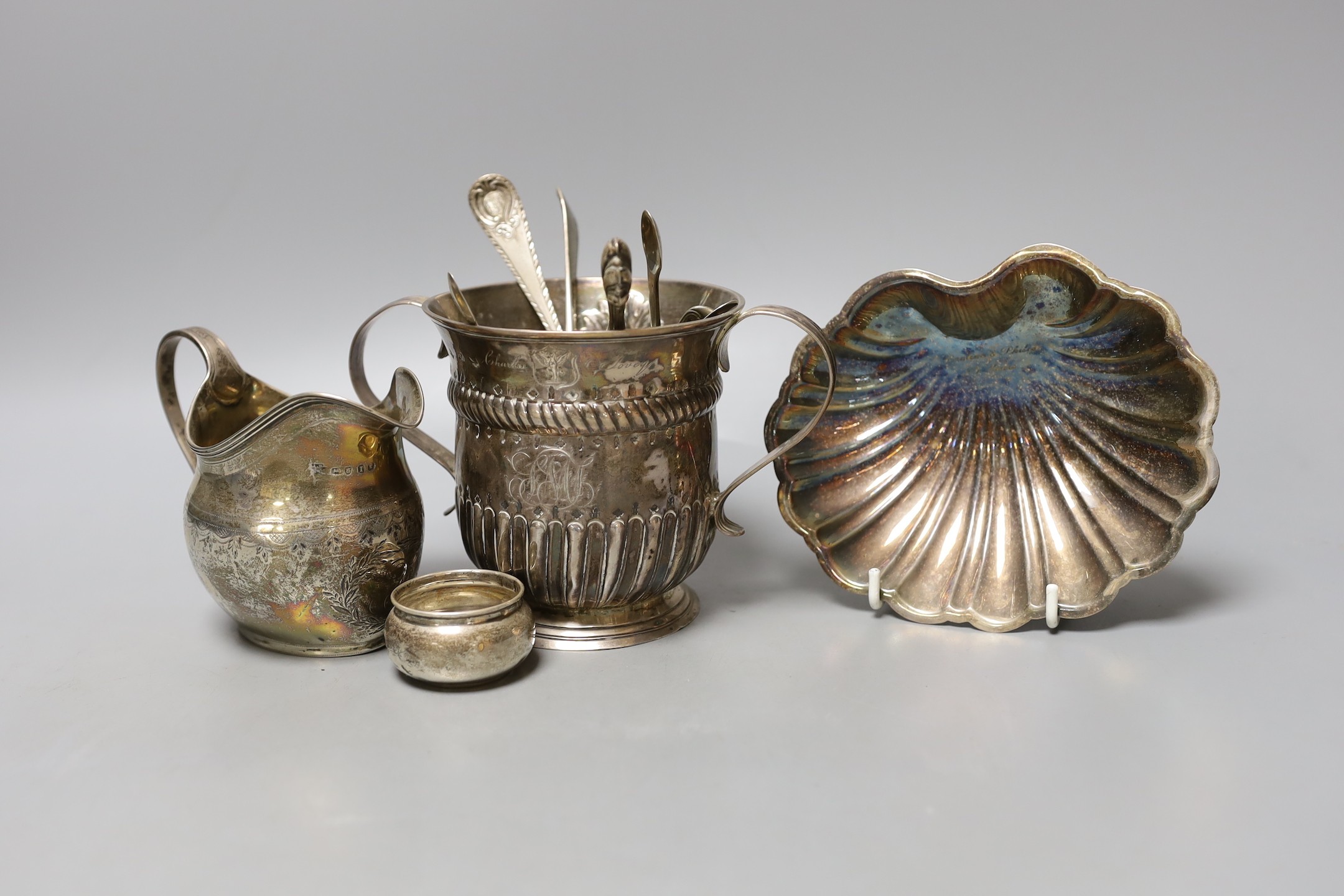 A George II silver porringer, London, 1748, 10.9cm, a George III silver cream jug, a silver shell dish, pair of silver tub salts, four items of silver flatware and two other items.